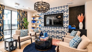 En moderne stue med et fjernsyn monteret på en væg med mønster, to sofaer med puder med mønster, et sofabord og en reol.