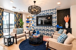 Ein modernes Wohnzimmer mit an einer gemusterten Wand montiertem Fernseher, zwei Sofas mit gemusterten Kissen, einem Couchtisch und einem Bücherregal.