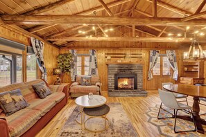 Ein Blockhaushaus-Interieur mit Kamin, Holzwänden, einer Couch, einem Esstisch und einer Kristallleuchter.