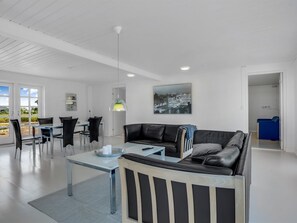 Ein modernes Wohnzimmer mit einem Glastisch, einer schwarzen Ledersofa, einer Essecke mit weißem Tisch und Stühlen sowie einem Stadtbild an der Wand.