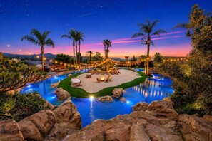 A pool area with lounge chairs, a fire pit, and palm trees at dusk. - Paradise Hills | A Lazy River Resort Estate (Valley Center)