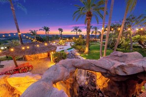 Ein Resort mit einer strohgedeckten Hütte, Sitzgelegenheiten im Freien, einem Pool, Palmen und Lichterketten.