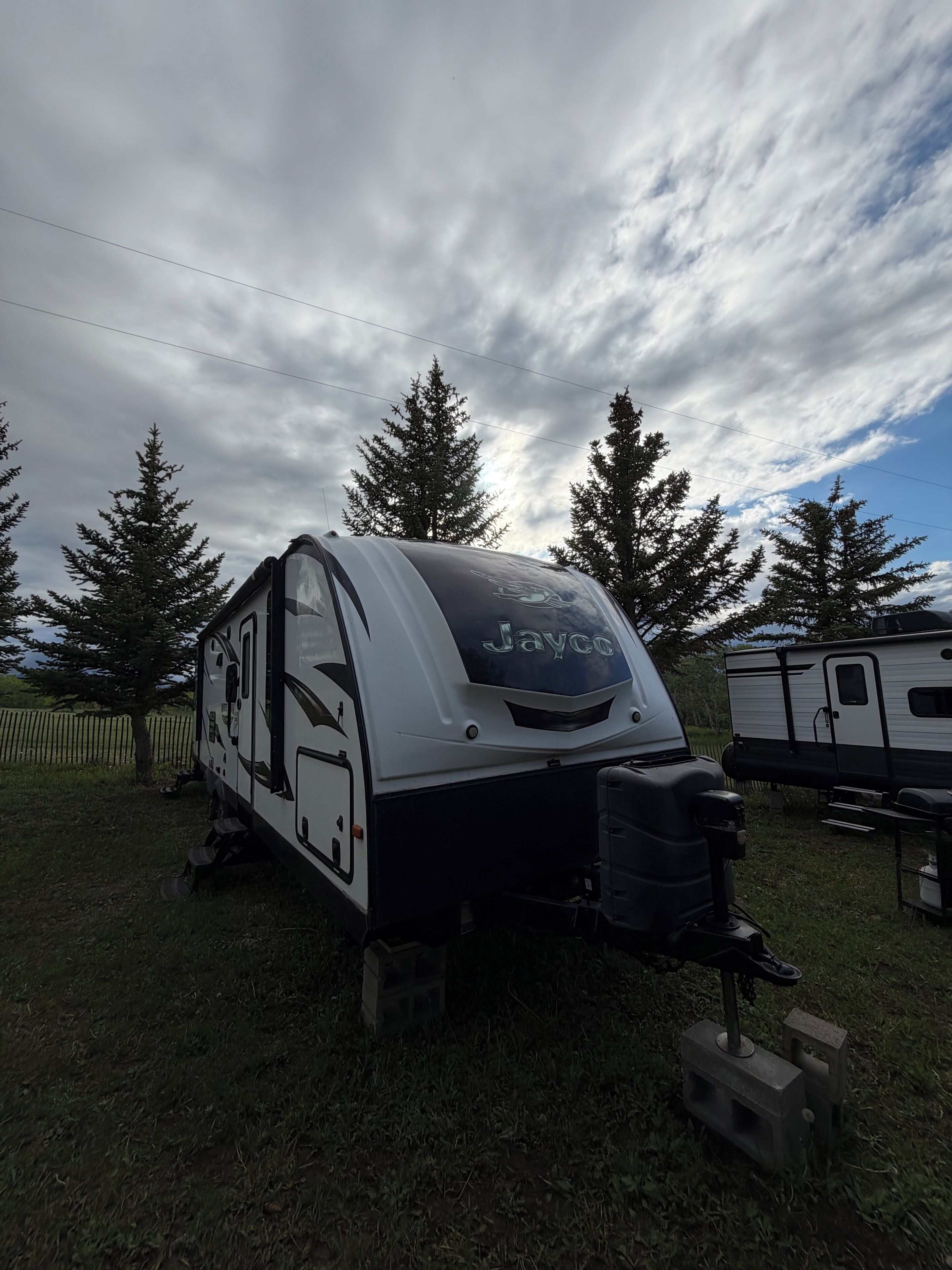 Een recreatiewagen (RV) met een Jayco logo, geparkeerd in een grasveld met bomen op de achtergrond.