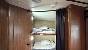 A compact room with a bunk bed, wooden wardrobe, and a ceiling light. - Montana Moon on the Lake "White Hawk" RV #3 (Babb)
