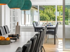 Ein moderner Essbereich mit einem langen Tisch, Stühlen und Blick auf Grünfläche.