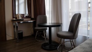 A hotel room with a desk, two chairs, a round table, a mirror, and a window with curtains.
