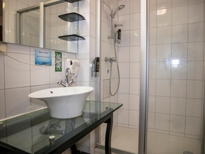 A bathroom with a white sink, a glass shower enclosure, and a mirror above the sink. - Patten (The Hague)