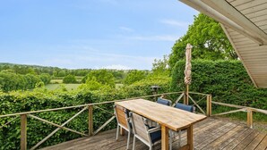 Um deck de madeira com mesa e cadeiras, com vista para uma paisagem verde.
