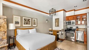 Une chambre d’hôtel avec un lit, un bureau, un coin cuisine et des tableaux encadrés au mur.