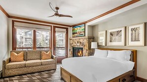 Une chambre à coucher avec un grand lit, une cheminée en pierre, un canapé et un ventilateur de plafond.