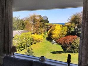 Ein Zimmer mit großem Fenster und Blick auf einen Garten mit verschiedenen Bäumen und einer Rasenfläche.