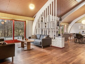 Ein modernes Interieur mit Holzboden, Kamin, Essbereich und großem Fenster mit Blick auf Bäume.