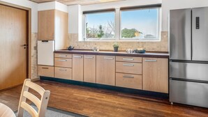 A modern kitchen with wooden cabinets, a stainless steel refrigerator, and a window with a view of trees. - "Stilla" - 19km from the sea by Interhome (Østervrå)