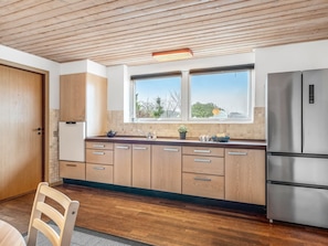 A modern kitchen with wooden cabinets, a stainless steel refrigerator, and a window with a view of trees. - "Stilla" - 19km from the sea by Interhome (Østervrå)
