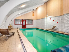 Ein Hallenbad mit gefliesten Wänden, Holzverkleidung und Liegestühlen.