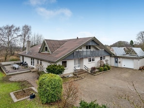 Ein zweistöckiges Haus mit überdachter Terrasse, Garage und einem kleinen, separaten Gartenhaus mit geneigtem Dach.