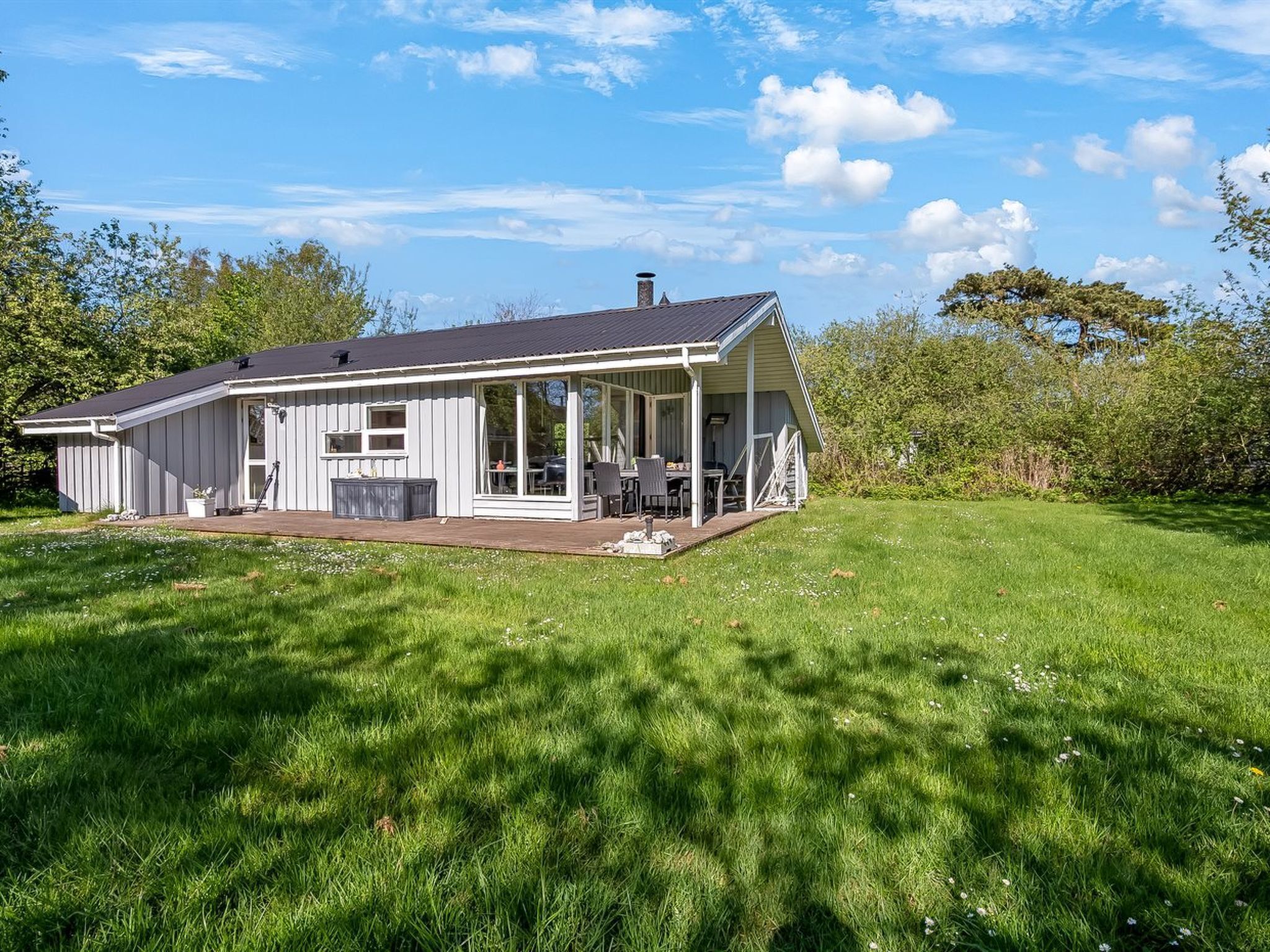 Ein eingeschossiges Haus mit einer Veranda, einer Terrasse und einem Rasen.