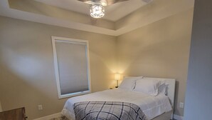 Ein Schlafzimmer mit einem Bett, einem Deckenventilator, einem Fenster mit Jalousien und einem Nachttisch mit Lampe.