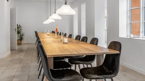 Ett konferensrum med ett långt bord i trä, svarta stolar, hängande taklampor och en vägg av tegelsten.