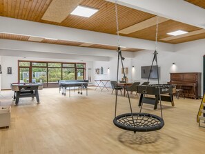 Un grand espace intérieur comprenant une table de ping-pong, un baby-foot et un fauteuil suspendu.