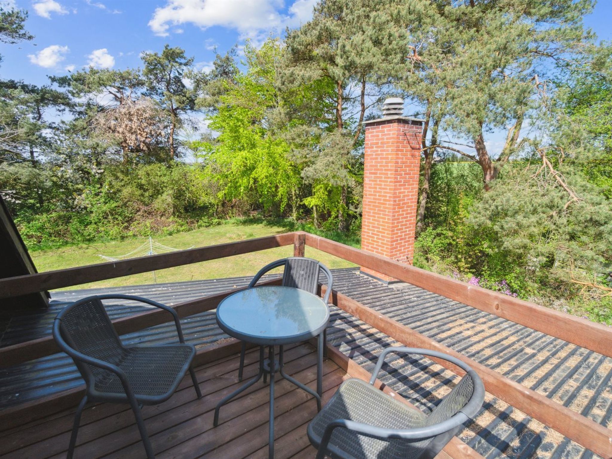 A deck with a brick chimney, wicker chairs, and a glass table.