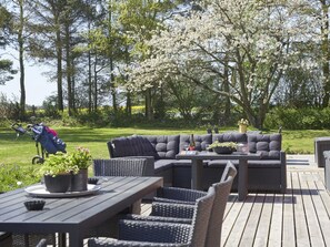 Eine Terrassenanlage mit einer dunkelgrauen Couch, Korbstühlen und einem Tisch.
