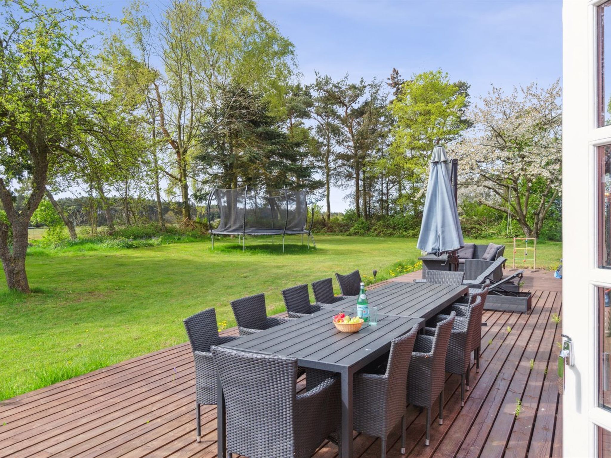 An outdoor deck with a dining table and chairs, surrounded by a grassy lawn and trees.