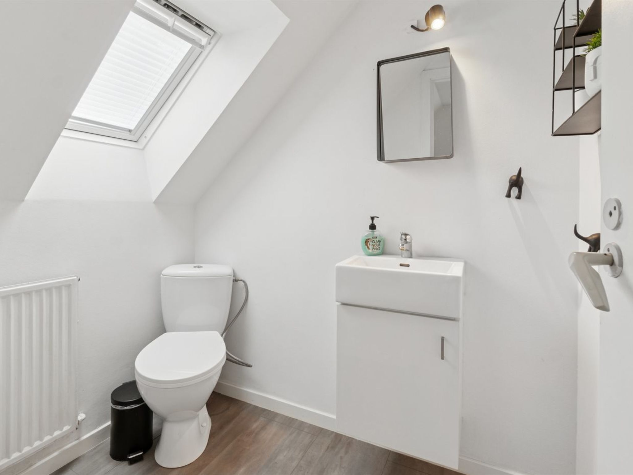 Een moderne badkamer met dakraam, witte sanitair en een klein spiegel.