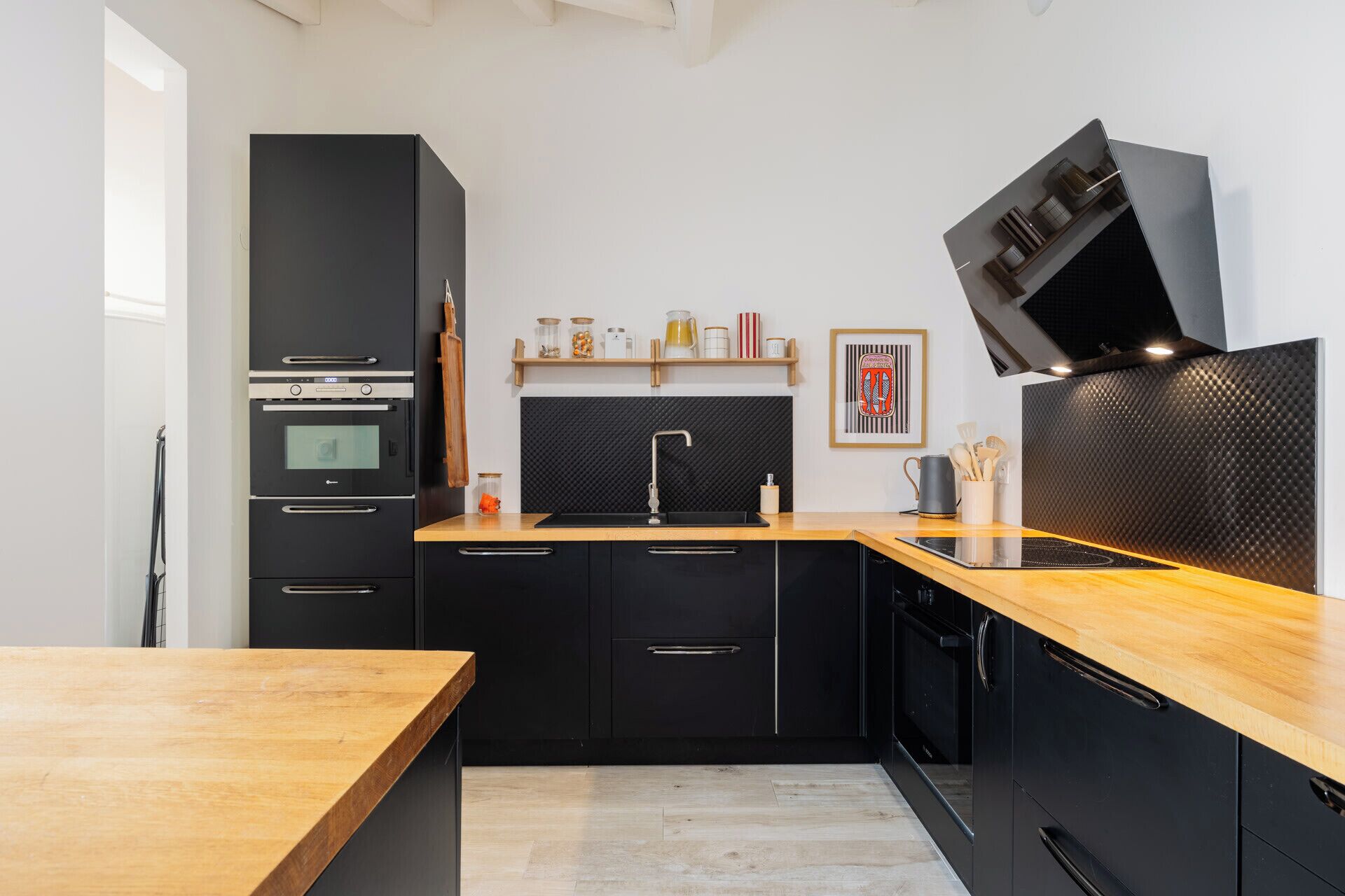 Een moderne keuken met zwarte kasten, een houten aanrecht, een inbouwoven, een spoelbak en een zwarte afzuigkap.