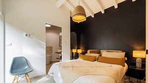 Ein Schlafzimmer mit Bett, Nachttischlampen, einem Sessel und einem durchgegangenen Tür sichtbaren Badezimmer.
