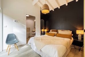 Ein Schlafzimmer mit Bett, Nachttischlampen, einem Sessel und einem durchgegangenen Tür sichtbaren Badezimmer.