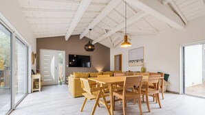 Ein modernes Interieur mit Essbereich, Sofa, Fernseher und großen Fenstern.