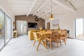Ein modernes Interieur mit Essbereich, Sofa, Fernseher und großen Fenstern.