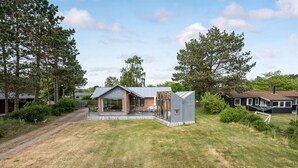 Une maison moderne dotée d’une grande baie vitrée, d’une terrasse en bois et d’une pelouse.