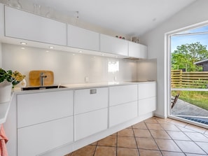 Eine moderne Küche mit weißen Schränken, einer Holz-Spritzschutzwand und einem großen Fenster mit Blick ins Freie.