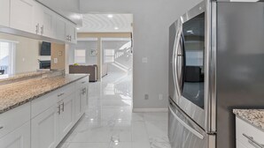 Une cuisine moderne avec des armoires blanches, un réfrigérateur en acier inoxydable et un sol en marbre.