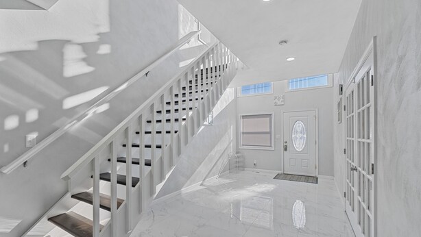 Un intérieur moderne avec un escalier, une porte ornée d’un panneau de verre décoratif et un couloir au sol carrelé.