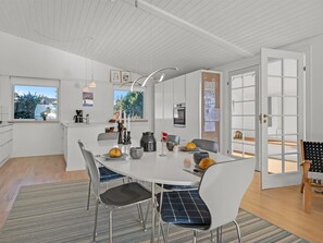 A modern kitchen with white cabinets, a dining table with chairs, and a view of the outdoors. - "Finelly" - 350m from the sea by Interhome (Ebeltoft)
