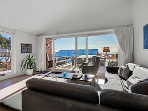 A modern living room with a sofa, coffee table, and a large window offering a view of a blue-roofed building. - "Finelly" - 350m from the sea by Interhome (Ebeltoft)