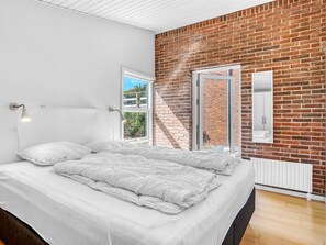 A bedroom with a large bed, a brick wall, a window, and a radiator. - "Finelly" - 350m from the sea by Interhome (Ebeltoft)