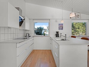 A modern kitchen with white cabinetry, a wooden floor, a large window, and a dining area with a bench. - "Finelly" - 350m from the sea by Interhome (Ebeltoft)