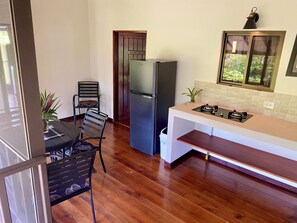 A compact kitchen with a refrigerator, a gas stove, a dining table with chairs, and a small potted plant. - 2-bedroom apartment in a hotel accommodating 2 to 4 people (Ojochal)