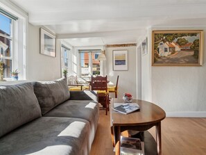 A modern living room with a sofa, dining table, and chairs, a painting on the wall, and a view of buildings outside. - "Ariela" - 150m from the sea by Interhome (Allinge)
