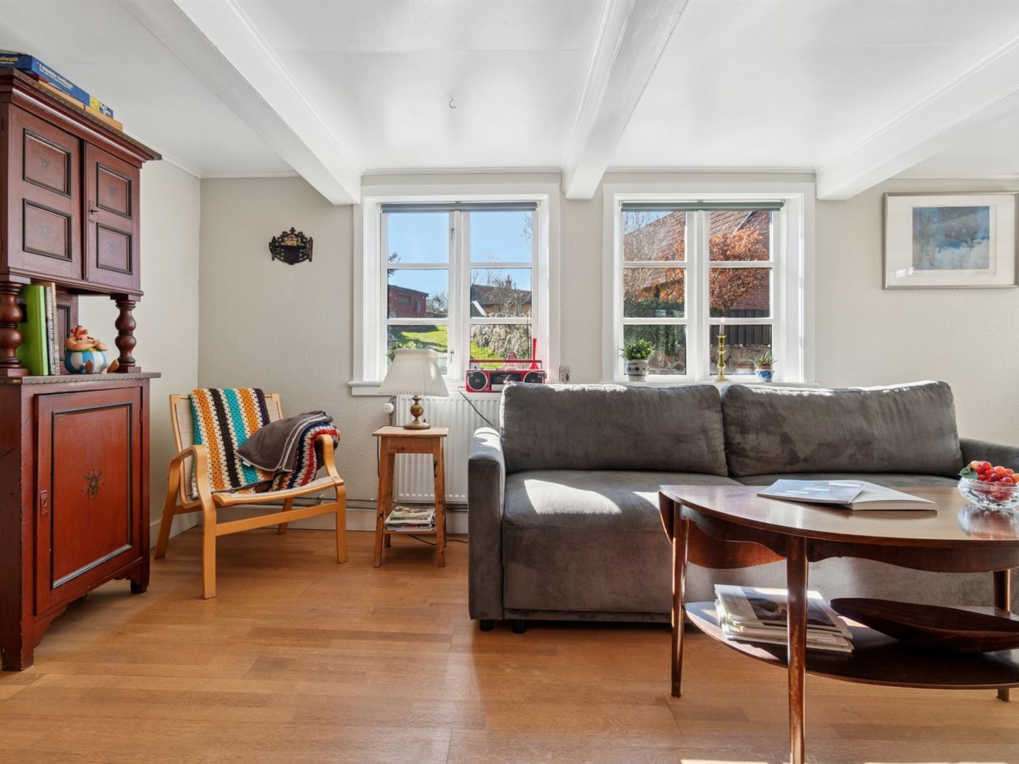 A cozy living room with a grey sofa, wooden floor, and a wooden cabinet with decorative items.