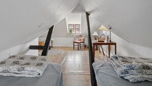 Ein Schlafzimmer im Loft-Stil mit schrägem Dach, zwei Betten mit gemusterten Bettbezügen, einem Holztisch, einem Stuhl und einem kleinen Tisch mit Lampe.