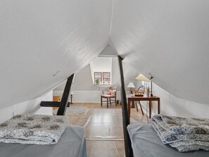A loft bedroom with a sloped ceiling, two beds with patterned bedding, a wooden desk, a chair, and a small table with a lamp. - "Ariela" - 150m from the sea by Interhome (Allinge)