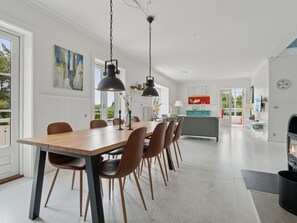 Ein geräumiger Essbereich mit einem langen Holztisch und modernen Stühlen, im Hintergrund eine Küche und ein Kamin.