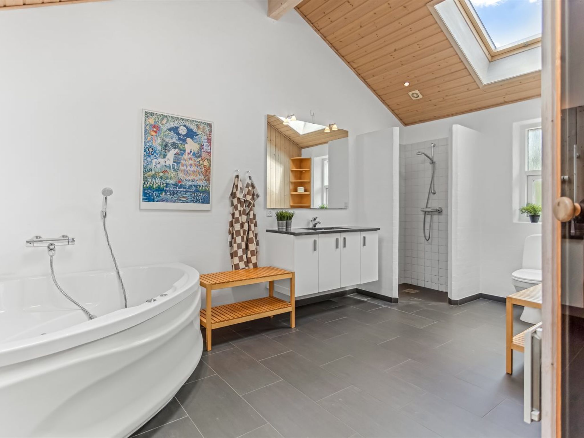 Une salle de bain moderne avec une baignoire sur pieds, un banc en bois, un grand miroir et une lucarne.