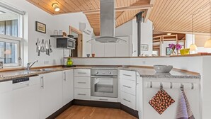 Moderni keittiö, jossa on valkoiset kaapit, sisäänrakennettu uuni ja puinen katto.