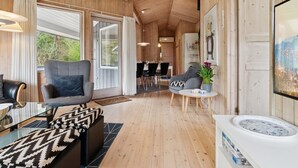 Ein modernes Interieur mit Holzwänden und Holzböden, einer Couch, einem Sessel, einem Essbereich und einem großen Fenster.